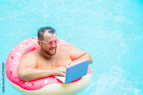 Wallpaper Mural enjoying Funny fat male in pink glasses on an inflatable circle in the pool works on a laptop portraying a girl. Torontodigital.ca