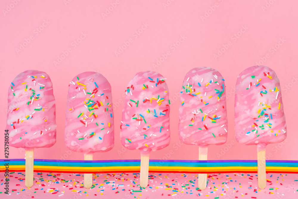 concept gay culture symbol with rainbow ribbons flag, sign LGBT community and unstable standing popsicle covered and strewed sprinkles on pink background concept gay culture symbol with rainbow ribbons flag, sign LGBT community and unstable standing popsicle covered and strewed sprinkles on pink background