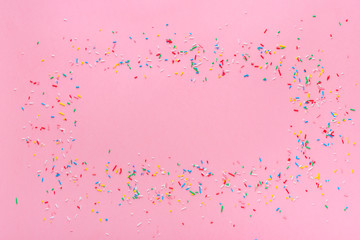 trendy frame of colorful sprinkles over pink background, decoration for cake and bakery