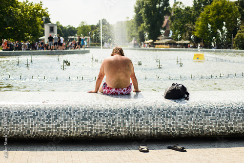 exhausted man cooling legs in fountain on hot summer day
