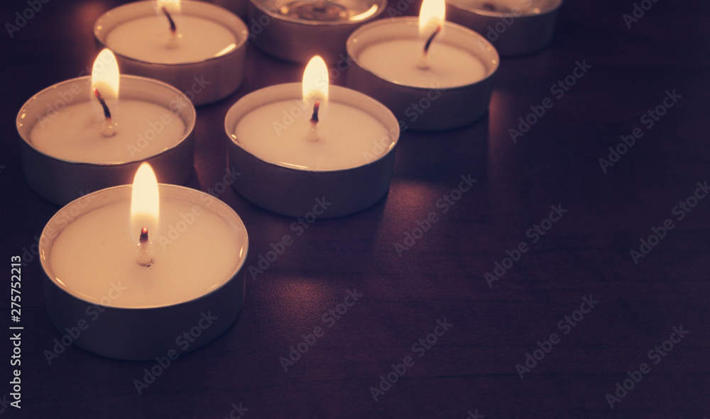 Many burning candle on table in darkness, closeup with space for text. Memorial symbol