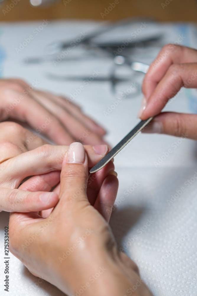 Top view manicurist polishing index finger for manicure in nail beauty salon. Step of manicure process. Manicure in beauty salon. Selective focus on costumer's nails. vertical photo Top view manicurist polishing index finger for manicure in nail beauty salon. Step of manicure process. Manicure in beauty salon. Selective focus on costumer's nails. vertical photo
