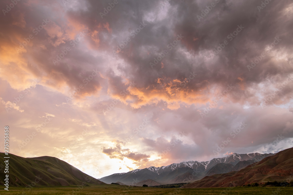 Sunset in the mountains of Tien Shan. Pastures on the background of snow-capped peaks of the mountain range.