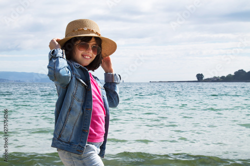 girl with hat and sunglasses walking along the shore of the beach photo
