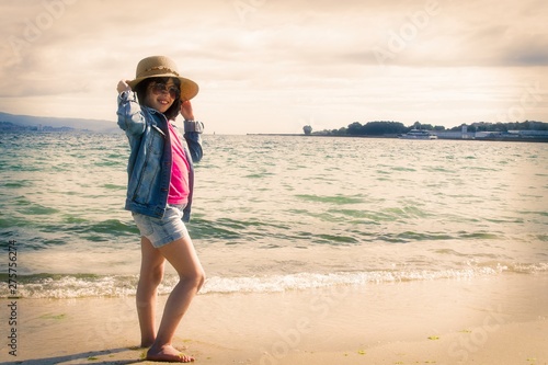 girl with hat and sunglasses walking along the shore of the beach