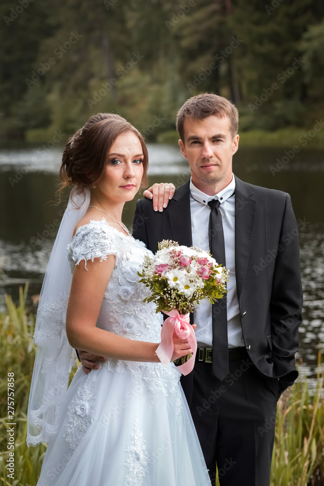 Portrait of wedding couple. Bride and groom embracing in the park against the background of the lake and forest. Sunny autumn day Portrait of wedding couple. Bride and groom embracing in the park against the background of the lake and forest. Sunny autumn day