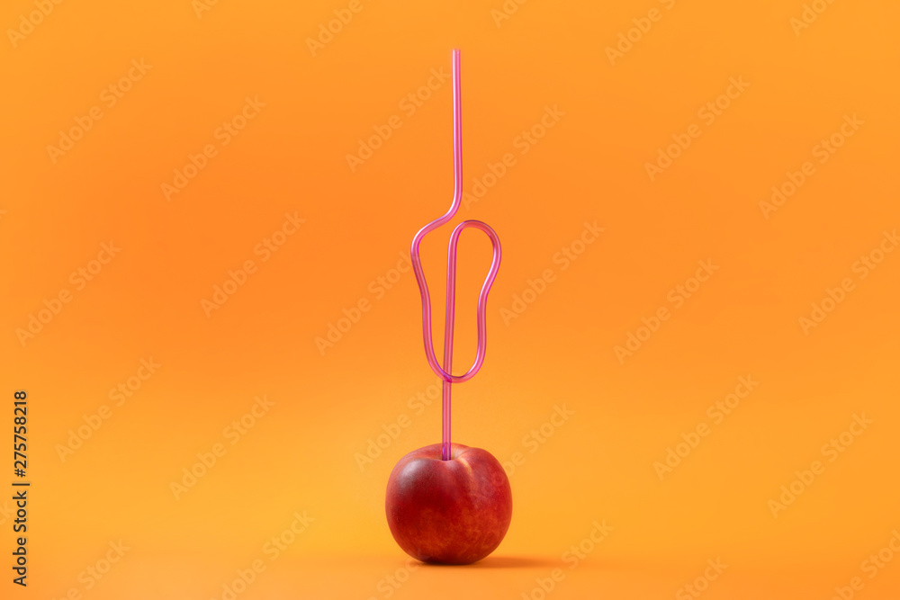 cocktail straw in peach on orange background, concept of juicy peach