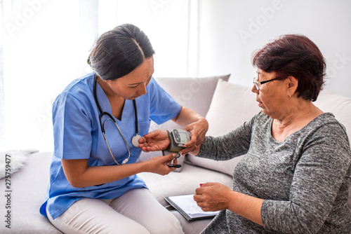 Asian Nurse Visiting Senior Woman For Check Up. Young nurse measuring blood pressure of elderly woman at home. Happy senior woman having her blood pressure measured in a nursing home by her caregiver