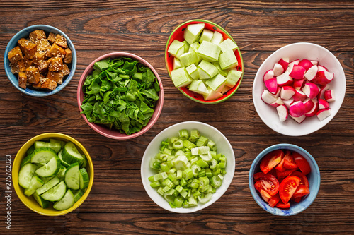 Ingredients of healthy nutrition in colorful bowls on a wooden table. Quinoa, raw vegetables and fried tofu