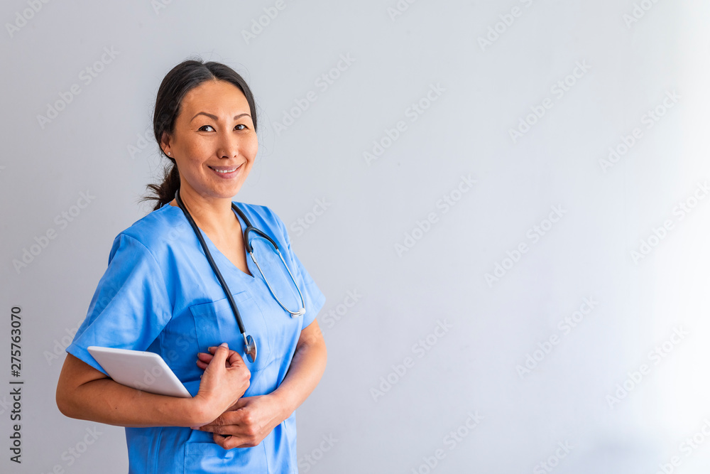 Nurse who is working her shift in a hospital. Close up portrait of female healthcare worker standing in hospital corridor. Asian woman in hospital hallway staring at camera. Nurse who is working her shift in a hospital. Close up portrait of female healthcare worker standing in hospital corridor. Asian woman in hospital hallway staring at camera.