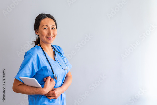 Nurse who is working her shift in a hospital. Close up portrait of female healthcare worker standing in hospital corridor. Asian woman in hospital hallway staring at camera. photo
