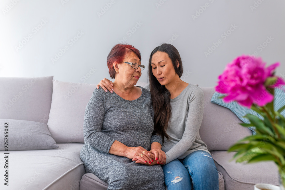 Love of mother and daughter. Smiling mother and daughter talking on couch at home. Asian Mother With Daughter Sitting On Sofa At Home Chatting