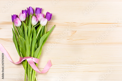 Bouquet of bright color tulips decorated with ribbon on wooden background. Top view  copy space