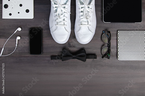 Modern men fashion accessories and electronic devices on dark background. White sneakers, tablet and phone flat lay
