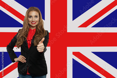 Portrait of happy pretty girl with thumb up on the UK flag background. Young woman learning english language and traveling in United Kingdom