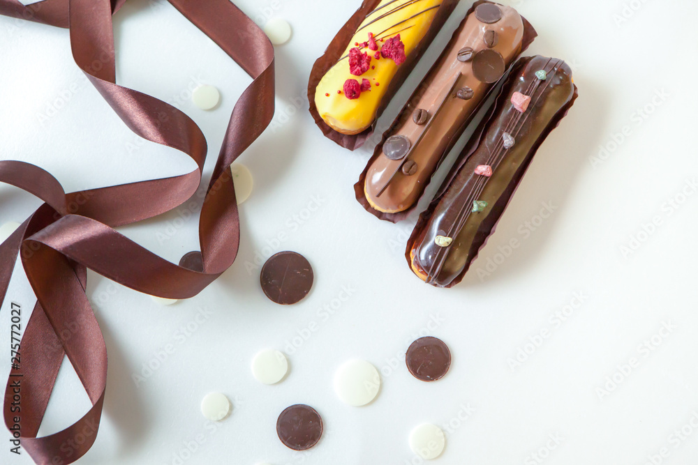 A set of three eclairs with different fillings and design isolate on a white surface decorated with chocolate drops and brown silk ribbon A set of three eclairs with different fillings and design isolate on a white surface decorated with chocolate drops and brown silk ribbon