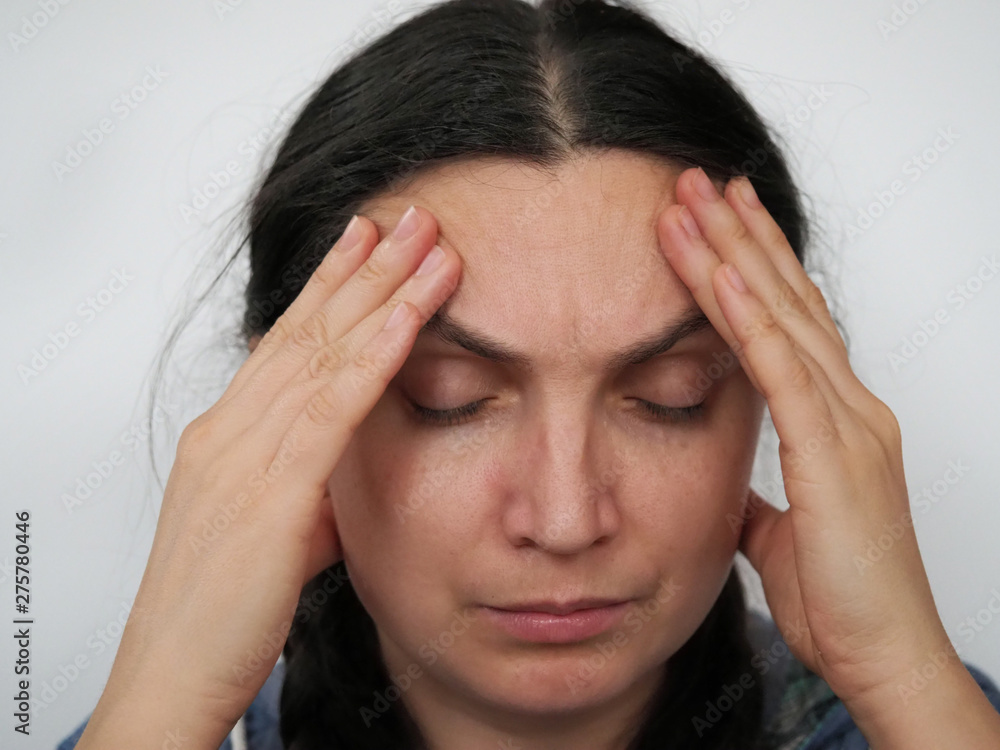 Fototapeta premium Emotional portrait of a woman close-up headache Close-up young beautiful woman holds her hands behind her head isolated on white background
