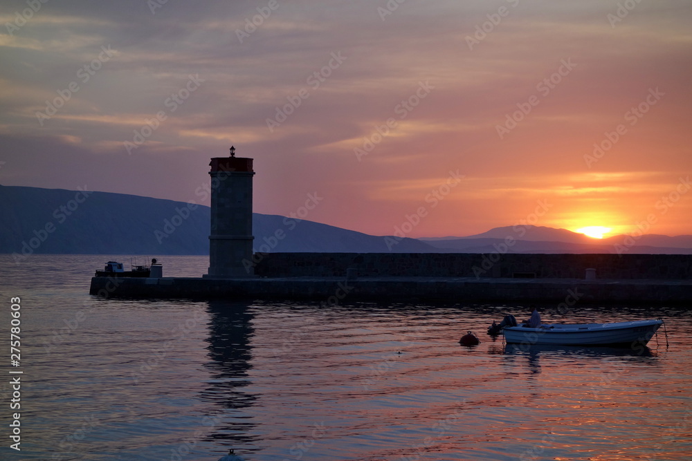 Sunset in Town of Senj, Primorje, Croatia. In the background lighthouse and fisherman in the boat.