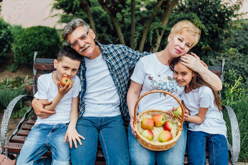 Grandparents sitting outdoors with their grandchildren  and smiling with basket apples.