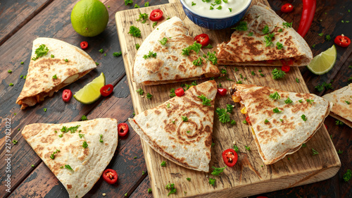 Mexican quesadilla with chicken, corn, black beans, cheese, vegetables, lime and yogurt sauce on wooden board photo