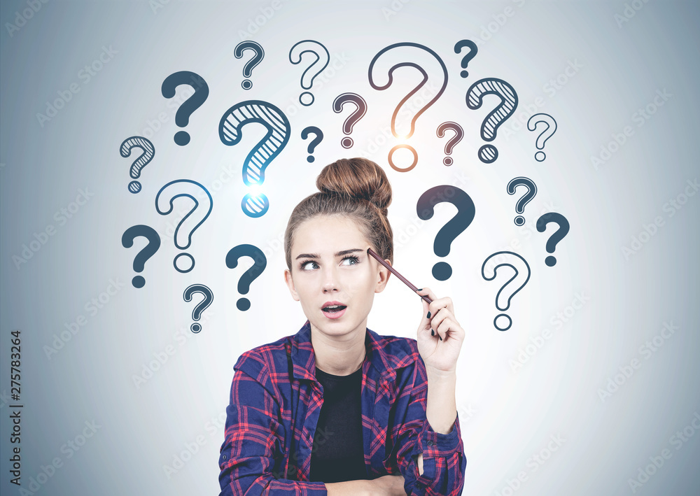 Thinking teen girl question marks on grey wall Thinking teen girl question marks on grey wall