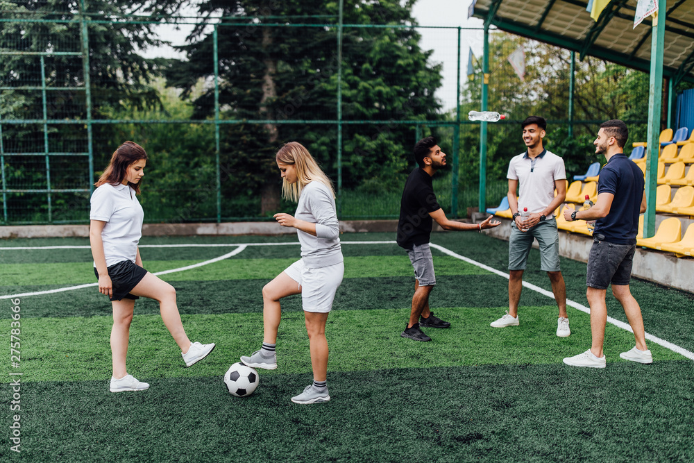 A group of friends in casual outfit play soccer in the open air. People have fun and have fun. Active rest and scenic sunset.