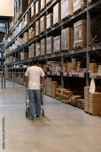 Buyer man with shopping cart in store between row of shelves with goods, shopping warehousing © pundapanda