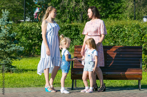 Women friends 35-40 years of age and small daughters 4-5 years of age are talking in park Two women with young children on the street.