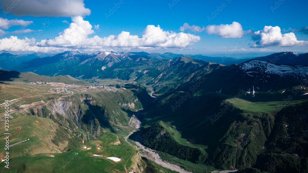 Aerial view of beautiful mountainous range and valley in Georgia. Mountains with snowy tops, blue sky, clouds.