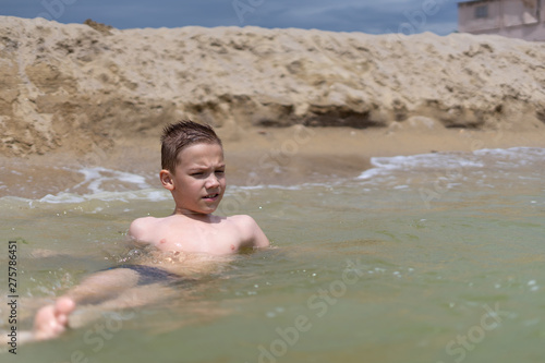 A boy of 9 years old is bathing and resting on a sandy beach by the sea.