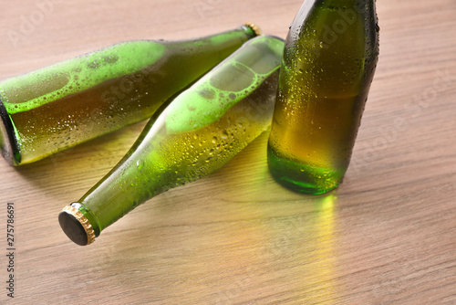 Three green bottles with alcoholic beverage on wooden table elevated