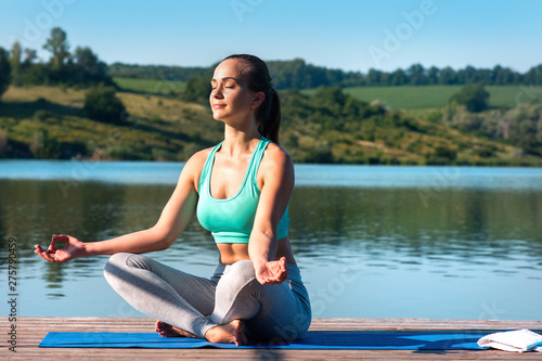 Beautiful girl practices yoga and meditates in the lotus position on the t the backdrop of beautiful nature