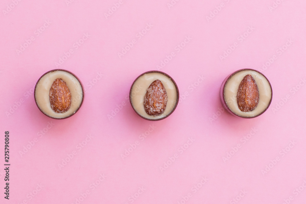 Three round chocolates with pistachio cream and salted almonds on pink background. Flat lay and copy space