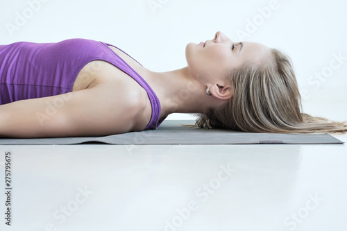 Caucasian woman practicing yoga, lying with eyes closed in Dead Body or Corpse pose, Savasana exercise, resting after yoga. Side view