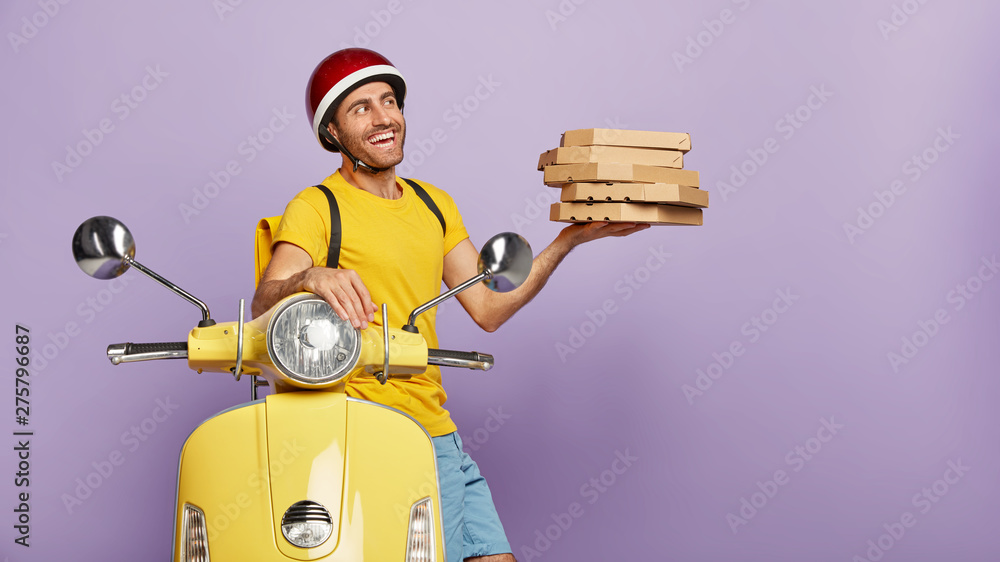Delivery service man holds pile of boxes with tasty pizza, reaches destination fast on motorcycle, wears protective helmet, has friendly outlook, brings order for customer. Food transporting concept - obrazy, fototapety, plakaty 