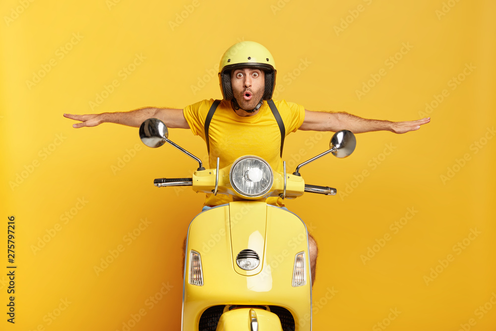 Shocked male motorcyclist travels on motorbike, has adventure trip and feels extreme, keeps hands away from handlebars, spreads sideways, likes active rest during summer, drives on high speed. - obrazy, fototapety, plakaty 