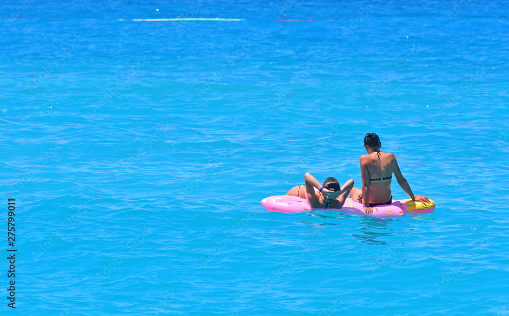 Two girls relax and sunbathe on a plastic inflatable sea air mattress