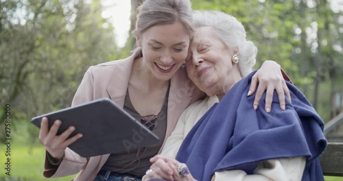 woman and senior grandmother using tablet device for video call at park.Granddaughter and grandma talking together with mobile.Active, caring,loving people relationship.slow motion video photo