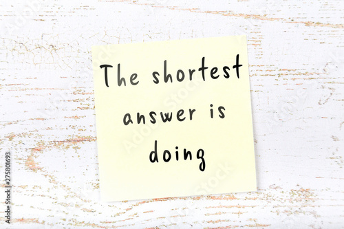 Yellow sticky note with handwritten wise quote on wooden wall  photo