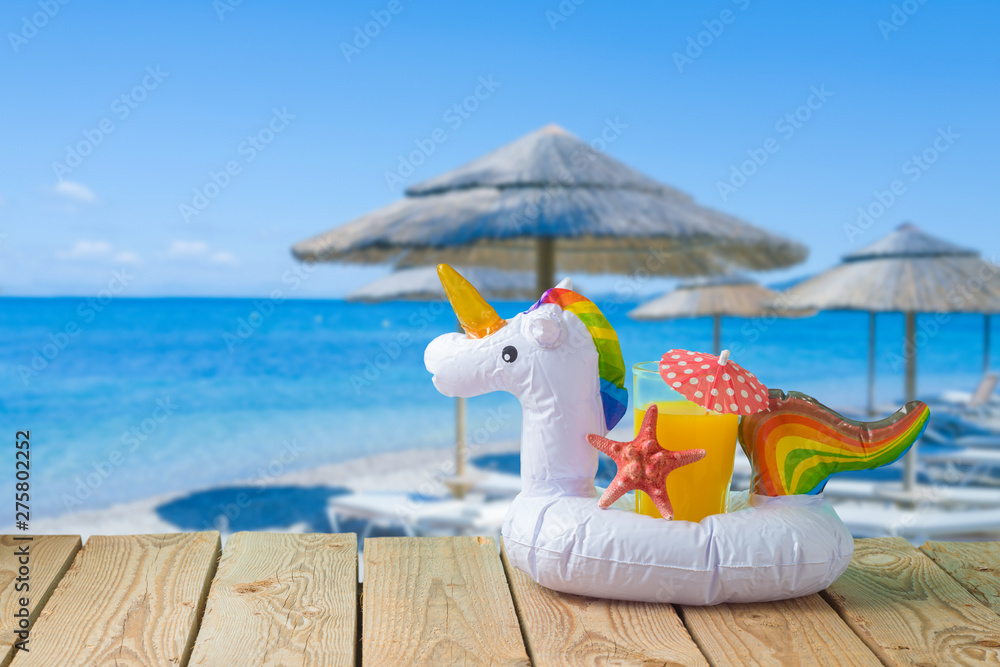 Summer vacation concept with orange juice and unicorn pool float over sea beach background