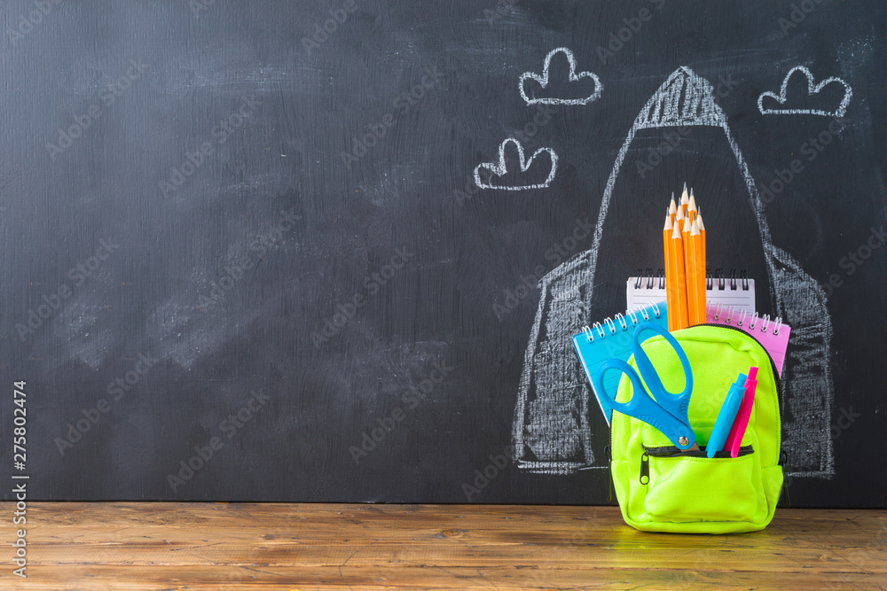 Back to school concept with small bag backpack, school supplies and rocket sketch over chalkboad background Back to school concept with small bag backpack, school supplies and rocket sketch over chalkboad background