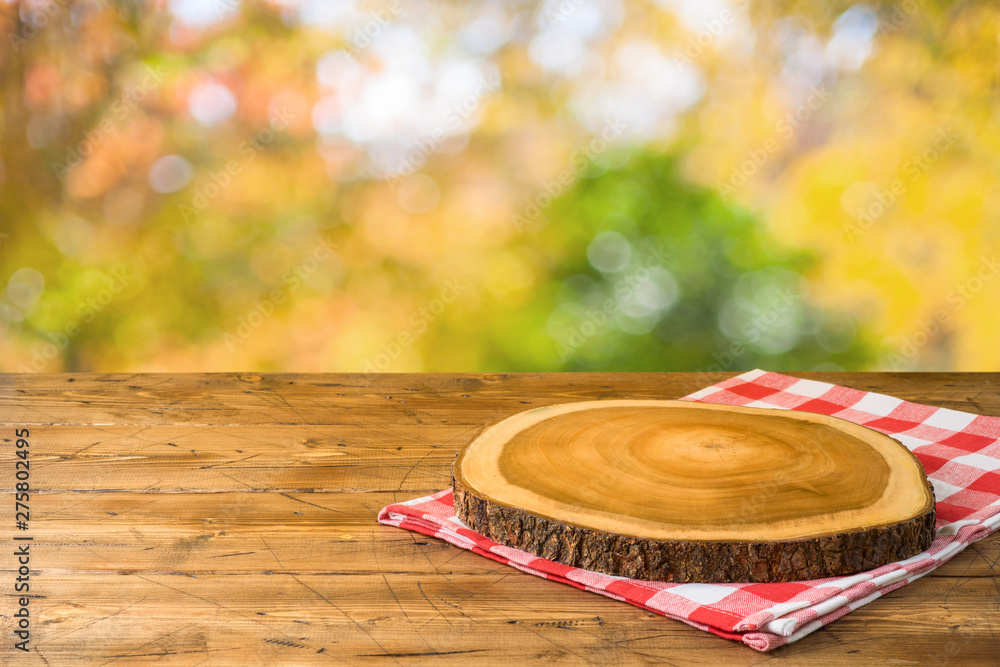 Obraz premium Empty wooden table with tablecloth and wooden board over autumn nature park background