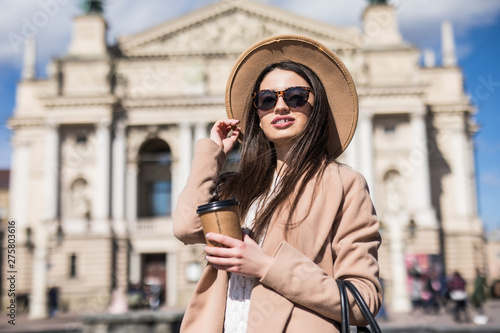 Coffee on the go. Beautiful woman holding coffee cup and smiling while walking along the street