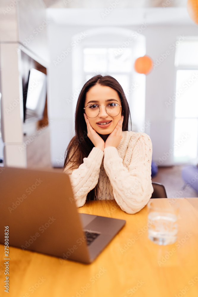 Charming young woman with a laptop looking into the camera in the kitchen Charming young woman with a laptop looking into the camera in the kitchen