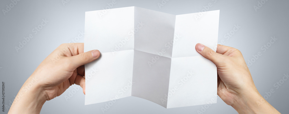 Obraz premium Hands holding a folded sheet of white paper on gray background