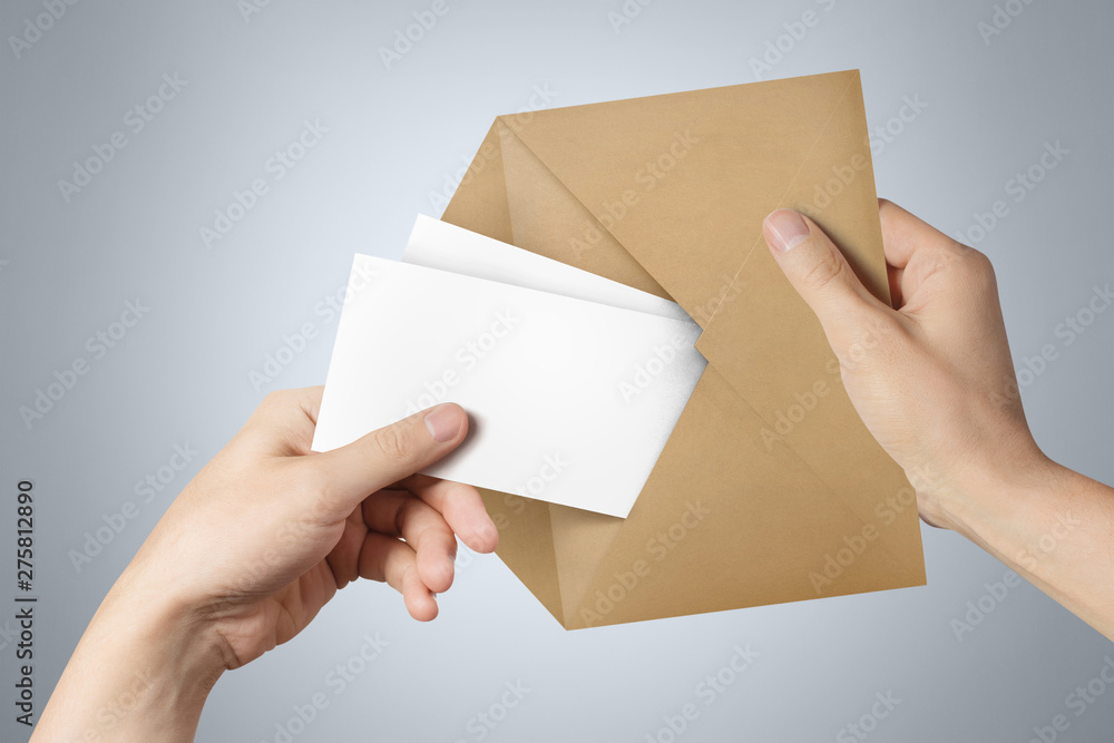 Fototapeta premium Hands pulling two blank sheets of paper (tickets, flyers, invitations, coupons, banknotes, etc.) out a brown envelope on gray background