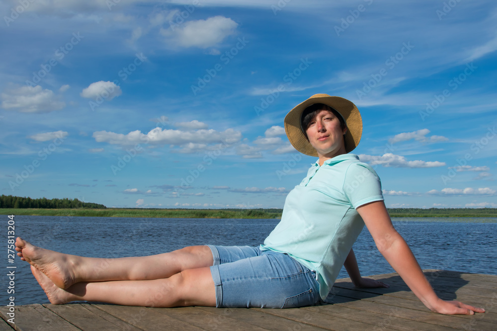 close-up, woman in a hat on a pier, is resting and enjoying a beautiful sky and lake