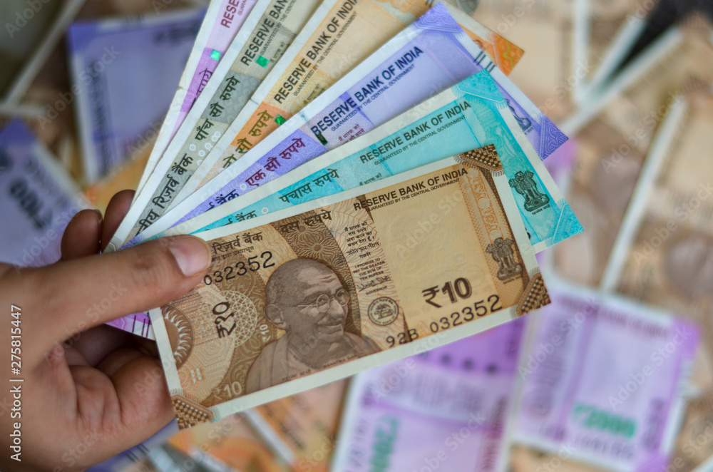Closeup of brand new colorful Indian currency bank notes of 10, 50, 100, 200, 500 and 2000 rupees bundle issued and in circulation after demonetisation held with hand with many notes in the background