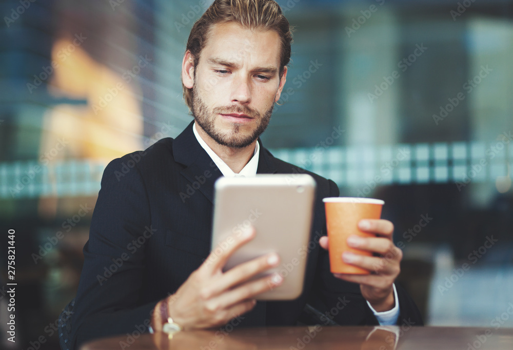 Handsome businessman enjoying a cup of coffee and looking his tablet Handsome businessman enjoying a cup of coffee and looking his tablet