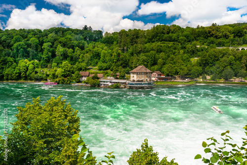 Beautiful, turquoise Rhine river flowing from a waterfall in northern Switzerland. Waterfall on the river Rhine. Visible boat and old castle on a small island.